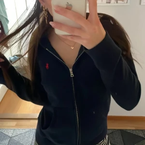 Mörkblå hoodie från Ralph Lauren - Säljer en snygg mörkblå hoodie från Ralph Lauren med dragkedja och det klassiska röda logotypbroderiet på bröstet. Perfekt för en casual look. Passar bra till jeans eller kjol💞