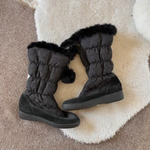 Svarta vinterstövlar från Coach - Snygga svarta vinterstövlar från Coach med pälsdetaljer och dragkedja. Har en liten defekt (se bild 2) men inget man direkt märker av. Saknar en sula. Storlek 36,5.