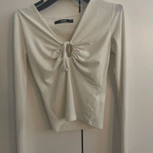 Vit långärmad topp från Bik Bok - Säljer en stilren vit långärmad topp från Bik Bok. Toppen har en v-ringad design med knytning framtill som ger en snygg detalj. Perfekt för att lyfta din outfit!