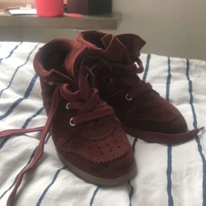 Vinröda sneakers från Isabel Marant - Snygga vinröda sneakers från Isabel Marant med snörning och perforerade detaljer. Skorna har en robust sula och är tillverkade i mocka för en lyxig känsla. Perfekta för att ge din outfit en trendig touch. Köpt second hand och använts en gång av mig men som nya