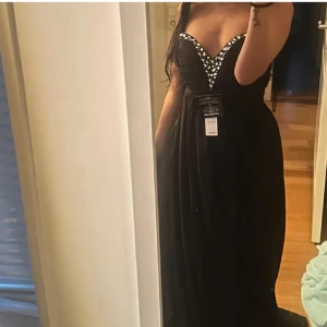 Svart bandeau långklänning NLY Eve - Ny oanvänd elegant svart axelbandslös klänning från Nelly Eve med silvriga diamant stenar längs den hjärtformade urringningen. Storlek XS men passar även S. Perfekt till bal eller andra fina tillfällen. 