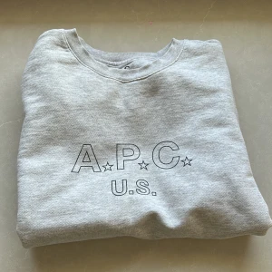 Grå sweatshirt från A.P.C. - Säljer en stilren grå sweatshirt från A.P.C. med tryck på framsidan. Tröjan har långa ärmar och en klassisk rund halsringning. Perfekt för en avslappnad look. Scick 9/10 då det finns väldigt få tecken på användning priset är ej hugget i sten
