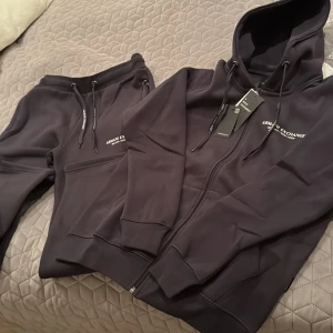 Svart set från Armani Exchange - Säljer en stilrent ljusare svart set från Armani Exchange. Hoodien är i storlek S medans byxorna är i storlek M med stora hål som går över skorna.