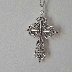 Silverfärgat korshalsband - Elegant silverfärgat halsband med ett detaljerat korshänge. Korset har intrikata mönster och små kuldetaljer som ger en vintagekänsla. Perfekt för att ge en stilfull touch till din outfit.