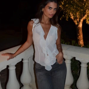 Vit ärmlös blus med volangdetaljer - Säljer en elegant vit blus med volangdetaljer framtill. Den är ärmlös och har en luftig passform. Storlek M/L men skulle säga att den är mer som en S. Aldrig använd 