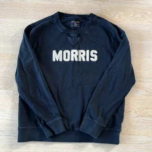 Svart tröja från Morris Gents - Säljer en svart tröja från Morris Gents med texten 'MORRIS' i vitt på framsidan. Tröjan har långa ärmar och en rund halsringning. Perfekt för en stilren och avslappnad look.