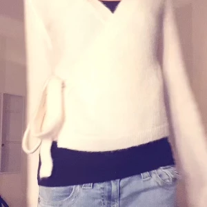 Vit omlott tröja från Gina Tricot  - Säljer en stilren vit omlott tröja med långa ärmar och knytband i sidan. Perfekt för en elegant och avslappnad look. Passar bra till jeans eller kjol. Köpt för 500kr