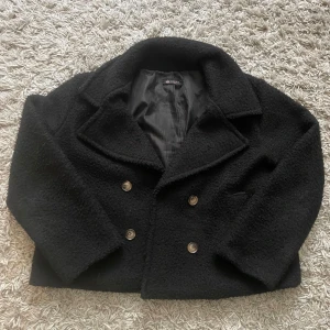 Svart teddykappa från Chelsea  - Säljer en snygg svart teddykappa från Chelsea Jackan har en dubbelknäppt design med stora knappar och en klassisk krage. Perfekt för våren och ger en trendig look. Storlek one size men är runt s/m. Mycket bra skick och köpt för 900.