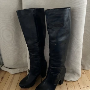 Svarta höga stövlar med klack - Snygga svarta stövlar i skinn med hög klack och dragkedja på insidan. Perfekta för en stilren look och passar bra till både kjol och byxor.