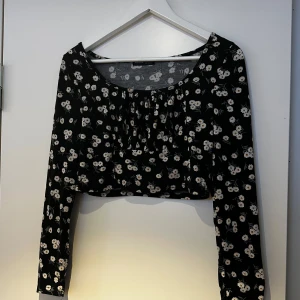 Svart blommig croppad topp - Säljer en svart croppad topp med vita blommor och långa ärmar. Perfekt för en trendig look. Toppen har en rund halsringning och är gjord i ett mjukt material. Tröjan är från shein 