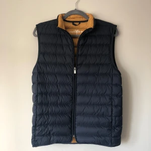 Mörkblå Väst - Snygg mörkblå dunväst med dragkedja. Perfekt för lager-på-lager. Västen har en stilren design och är lätt att matcha med olika outfits.