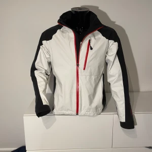 Vit och svart jacka från Galvin Green - Säljer en stilren vit och svart jacka från Galvin Green med röd dragkedja. Super skön och vind och vatten tät plus riktigt fet