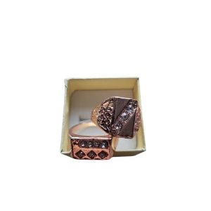 Rosefärgade ringar med glittriga detaljer - Två eleganta rosefärgade ringar med glittriga stenar. Den ena ringen har en rektangulär design med rader av stenar, medan den andra har ett diagonalt mönster med gnistrande stenar. Perfekta för att ge en touch av glamour. US 11 eller 20.6 mm