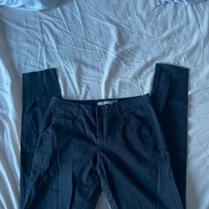 Svarta byxor från Bershka - Snygga svarta byxor från Bershka med en klassisk design. De har en normal passform och är perfekta för en stilren look. Byxorna har fickor fram och bak samt knappar för stängning.