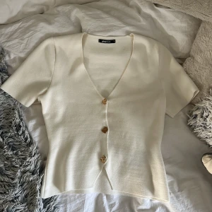 Vit kortärmad kofta från Gina Tricot - Säljer en stilren vit kofta från Gina Tricot med korta ärmar och v-ringning. Koftan har tre dekorativa knappar framtill som ger en elegant touch. Perfekt för en chic och enkel look. Nypris 399, säljer för 270💗oanvänd 