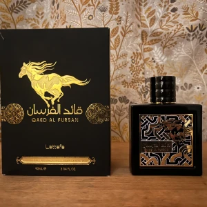 Qaed Al Fursan Eau de Parfum från Lattafa - Qaed Al Fursan från Lattafa är en elegant parfym med en fruktig och söt doftprofil. Flaskan är svart och fyrkantig med ett gyllene hästmotiv. Den har noter av trä, tropiska frukter och en varm kryddighet, vilket ger en unik och lockande doftupplevelse.