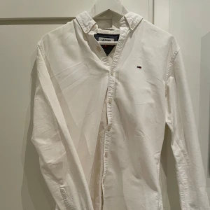 Vit skjorta från Tommy Hilfiger - Snygg vit skjorta från Tommy Hilfiger med klassisk design och liten logotyp på bröstet. Skjortan har långa ärmar och knappar framtill. Perfekt för en stilren look. Nypris 699kr