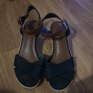 Blå kilklackssandaler med bruna remmar - Snygga blå sandaler med kilklack och bruna justerbara remmar. Perfekta för sommarens alla tillfällen. Sandalerna har en bekväm passform och en stilren design.