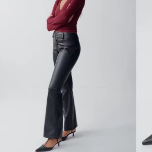 Svarta skinnbyxor - Snygga svarta skinnbyxor med bootcut-stil. De har en hög midja och en stilren design som passar perfekt för en trendig look. Byxorna har en dragkedja och knappar framtill. Dessa har aldrig använts pgd av att de har suttit för stort! Slutsålda på hemsidan🥰