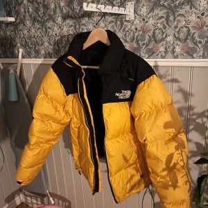 Gul och svart dunjacka från The North Face - Säljer en cool gul och svart dunjacka från The North Face. Jackan har en pufferdesign med dragkedja och hög krage för extra värme. Perfekt för kalla dagar och har en snygg logga på bröstet och ryggen. En riktig statement piece för vintern! 🖤💛Pris går att förhandla. 