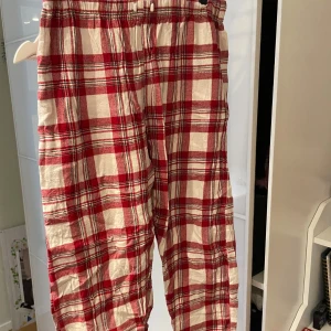 Röd- och vitrutiga byxor - Säljer ett par mysiga röd- och vitrutiga byxor med elastisk midja. Perfekta för en avslappnad dag hemma. Byxorna har en klassisk rutig design som ger en tidlös look. Köpta på Åhléns Outlet. 