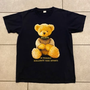 ”Believe in yourself” P-K - Säljer en svart t-shirt med ett nallemotiv och texten 'Believe in yourself, Xcellerate your efforts'. Från P-K. Perfekt för en avslappnad stil. T-shirten har korta ärmar och är gjord i bomull. Provad på annars i Nyskick. Storlek Small. Längd 65cm Bredd 48,5cm.