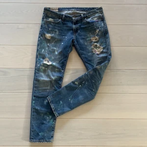 Ralph lauren jeans - Säljer ett par blå jeans från ralph lauren med snygga slitningar och färgstänk för en unik look. Perfekta för dig som vill ha en avslappnad och trendig stil. Nypris 2500