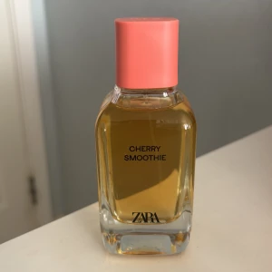 Cherry Smoothie parfym från Zara - Säljer en oanvänd elegant parfymflaska från Zara med doften Cherry Smoothie. Flaskan har en rektangulär form med en ljusrosa kork och genomskinligt glas som visar den gyllene vätskan inuti. Perfekt för den som älskar fruktiga och söta dofter.