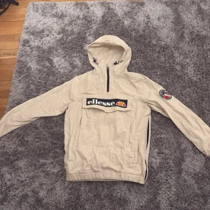 Beige jacka från Ellesse - Säljer en beige jacka från Ellesse med huva och dragkedja. Jackan har en stor ficka framtill med Ellesse-logga och ett broderat märke på ärmen. Perfekt för en sportig look! Man kan använda den till även att åka skidor är använd 3 gånger. Pris går att diskutera 