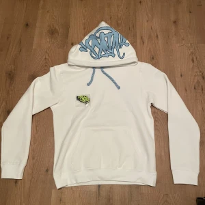 Vit hoodie med blå text - OBS: byxor finns även att köpa med. Byxorna finns även tillgänglig att köpa med, vid köp av hela tracksuiten så blir priset billigare 