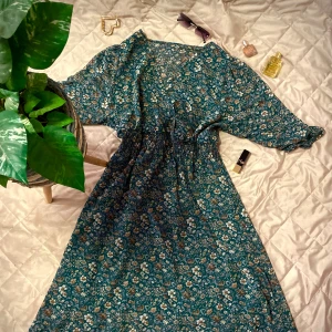 Blommig grön klänning - Säljer en vacker grön klänning med blommigt mönster. Klänningen har en v-ringad design och trekvartsärmar. Perfekt för en somrig look med sin luftiga passform och elastiska midja. Pris går ty diskutera!