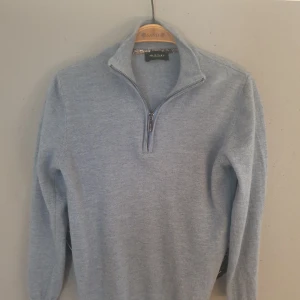 Grå tröja med dragkedja från Sand Copenhagen - Säljer en stilren grå tröja från Sand Copenhagen med halv dragkedja och hög krage. Perfekt för kyligare dagar och passar bra till både jeans och chinos. Tröjan har långa ärmar och är tillverkad i ett mjukt material.