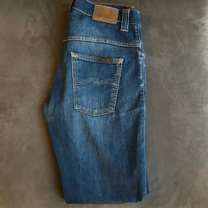 Blå jeans från Nudie Jeans - Snygga blå jeans från Nudie Jeans med klassisk femficksdesign och subtila broderier på bakfickorna. Modellen heter Thin Finn och är tillverkad i 98% ekologisk bomull och 2% elastan för en bekväm passform. Perfekta för en avslappnad stil.
