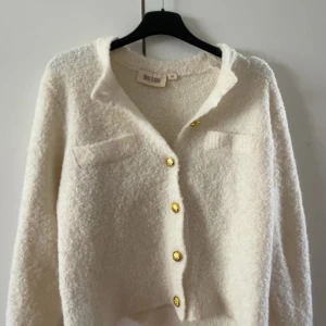 Vit kofta från Ullared  - Säljer en mysig vit kofta från Ullared med gyllene knappar framtill. Koftan har en mjuk textur och långa ärmar, perfekt för kyliga dagar. Den har också två dekorativa fickor på bröstet. Perfekt för att hålla stilen och värmen! 🤍