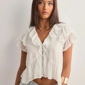 Vit blus med volanger - Säljer en söt vit blus från Nelly med volanger och v-ringning. Blusen är alldeles ny och har pris laggen kvar !