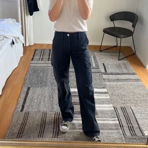 Mörkgrå cargobyxor - Snygga gråa cargobyxor med flera fickor och en bekväm passform. Byxorna har en hög midja och raka ben. Fickorna på baksidan är inga riktiga fickor. 