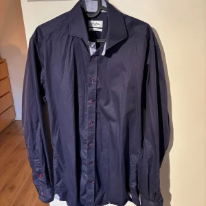 Mörkblå skjorta från Stenströms - Snygg mörkblå skjorta från Stenströms i slim fit. Tillverkad av tvåfaldig super bomull för en lyxig känsla. Skjortan har långa ärmar och röda knappar som ger en fin kontrast. Perfekt för en stilren look.