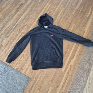 Svart Comme des Garçons PLAY hoodie - Svart hoodie från Comme des garcons play. Är lite använd och är köpt från vinted för ett halvår år sedan för 1000 passar tröjan passar både tjejer och killar och storleken är medium men passar s och xs några små hål därför kostar den lite men de ser man knappt går enkelt att laga snörena är också borta. Men annars en riktig snygg tröja