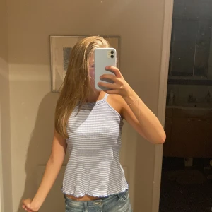 Randig blåvit linnetopp med smala axelband - Säljer en söt och somrig linnetopp med smala axelband och rundad hals. Toppen är blåvit med tunna horisontella ränder och har vågig kant nertill. Perfekt till jeansshorts eller kjol för en chill look.