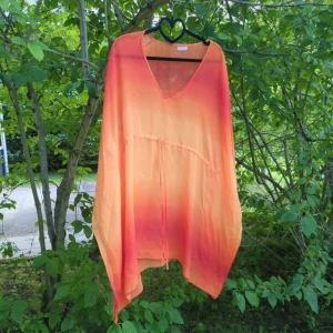 Orange-röd blus från Sloggi onesize - Säljer en flowy och transparent blus från Sloggi i en snygg orange-röd ton. Modellen är loose fit med v-ringning och knytband framtill. Perfekt för strandhäng eller chill dagar. Materialet är lätt och luftigt, vilket gör den superbekväm under varma dagar. Katter finns i hemmet.