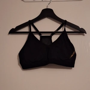 Svart sportig träning-bh från Newbody - Svart träning-bh från Newbody med smala axelband och snygg meshdetalj i ryggen. Toppen har en sportig look och är perfekt för träning. Mjukt och stretchigt material som sitter skönt på kroppen. ⚠️Osäker på om storleken är S eller M⚠️