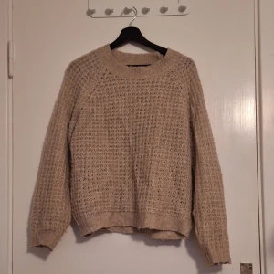 Beige stickad tröja med grov struktur - Beige stickad tröja med grov, luftig struktur och bred ribbad mudd vid hals, ärmslut och nederkant. Långärmad och lite oversized fit, perfekt för lager-på-lager. Enkel att matcha med jeans eller kjol för en chill look.