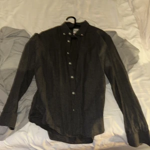 Mörkgrå henley-skjorta från Dobber - Snygg mörkgrå henley-skjorta från Dobber med lång ärm och klassisk knappslå framtill. Skjortan har en rak passform och är tillverkad i mjukt bomullstyg. Perfekt för dig som gillar stilrena och enkla plagg.