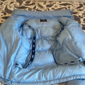 Ljusblå pufferjacka från Hoodrich XS - Säljer en ljusblå pufferjacka från Hoodrich i storlek XS. Jackan har huva, dragkedja framtill och stora broderade loggor både fram och bak. Fodrad och riktigt fluffig, perfekt för kalla dagar. Snygga svarta detaljer på insidan och två fickor framtill. Pris kan diskuteras 