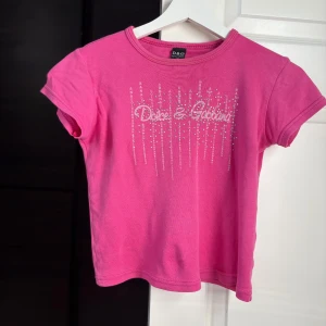 Rosa Dolce & Gabbana t-shirt med strass - Snygg rosa t-shirt från Dolce & Gabbana med korta ärmar och glittrande strassdetaljer framtill. Inte säker på om den är äkta.