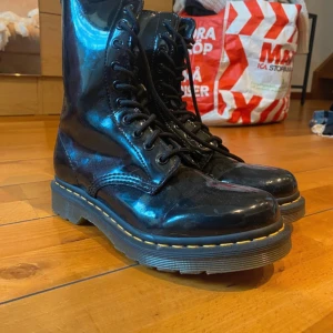 Svarta Dr. Martens boots lack - Säljer ett par svarta Dr. Martens boots i glansigt lackskinn med klassisk gul söm runt sulan. Skorna har snörning framtill, dragkedja på sidan. Är använda max 10 gånger, nypris var 1400. Storlek 38/39