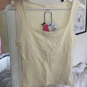 Ljusgul linnetopp från Selected Femme - Supersöt ljusgul linnetopp från Gina Tricot med breda axelband och fyrkantig ringning. Toppen är i mjuk bomull och har en clean, enkel look som är lätt att matcha. Perfekt för varma dagar och ger en fräsch vibe till din outfit.