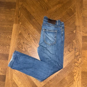 Love Moschino blå jeans slim fit - Säljer ett par blå jeans från Love Moschino med slitna detaljer och snygg tvätt. Jeansen har klassisk femficksdesign, smal passform och normal midja. Materialet är mjukt denim i bomull med lite stretch för extra komfort.