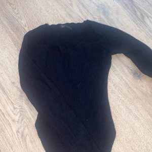 Svart ribbad stickad tröja SHE - Svart stickad tröja från SHE med ribbad struktur och långärmad design. Tröjan har en snygg, figurnära passform och rund halsringning. Perfekt för dig som gillar stilrena och enkla plagg med lite edge.