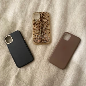 Tre mobilskal i svart, brunt och leopard - Säljer tre snygga mobilskal: ett svart med gulddetalj runt kameran, ett brunt i matt finish och ett transparent skal med leopardmönster och glittriga inslag. De passar iPhone 11 och alla är från H&M💕. Alla 3 skal för 120, 1 för 50💕 *de svarta skalet är lite sönder på kanten men inget som man tänker på.